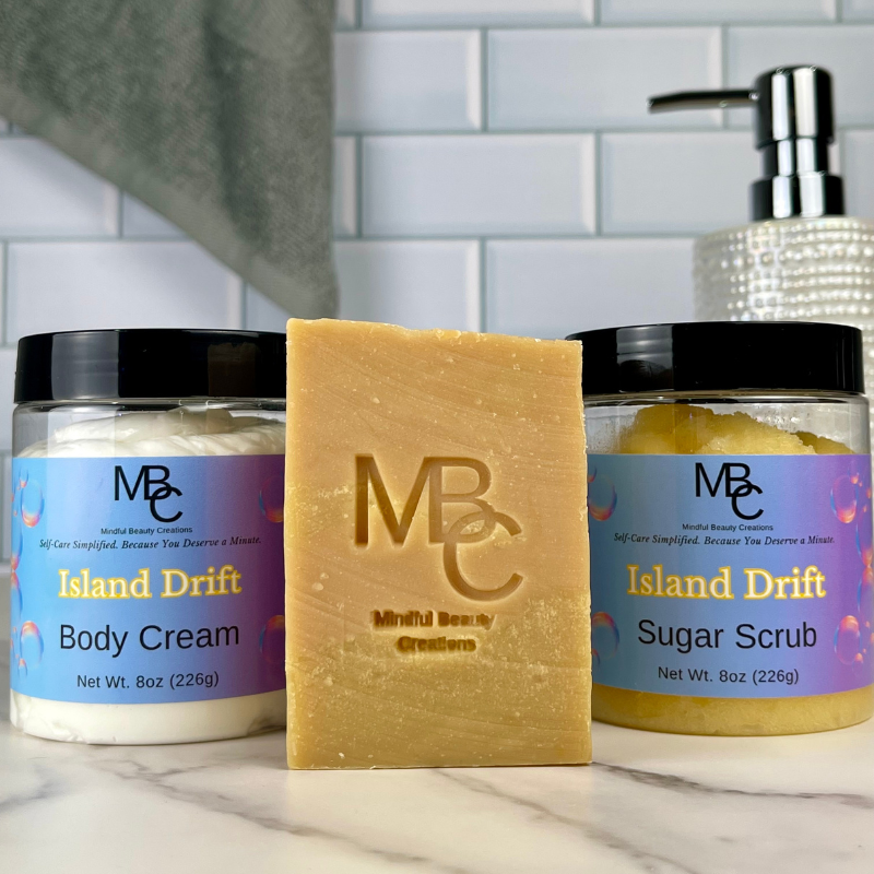 Two jars of 'Island Drift' body cream and sugar scrub with a bar of soap on a bathroom counter.