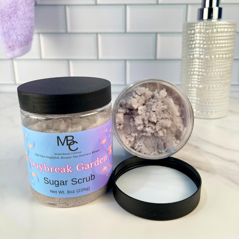 Daybreak Garden Sugar Scrub jar with open lid showing scrub and cream on a white surface.