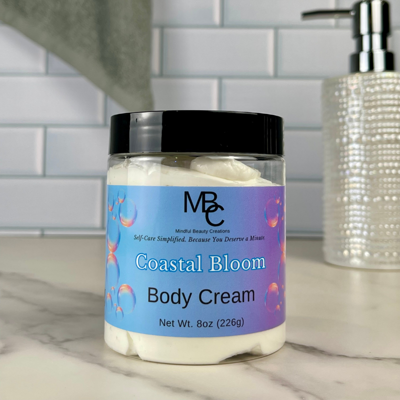 Jar of Coastal Bloom Body Cream with a blue label on a marble surface.