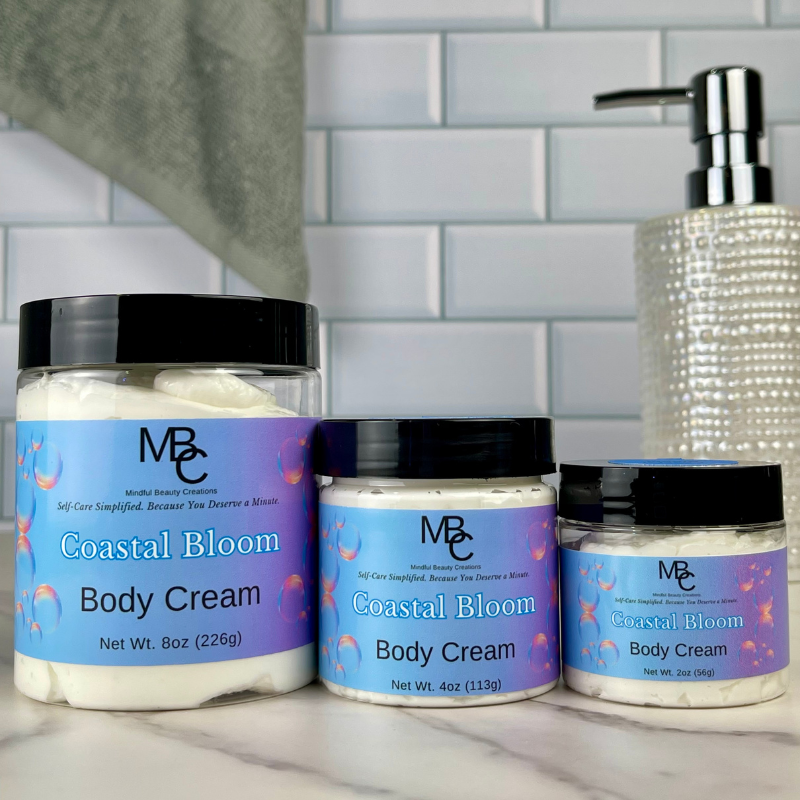 Three containers of Coastal Bloom Body Cream on a bathroom counter with a tiled wall background.