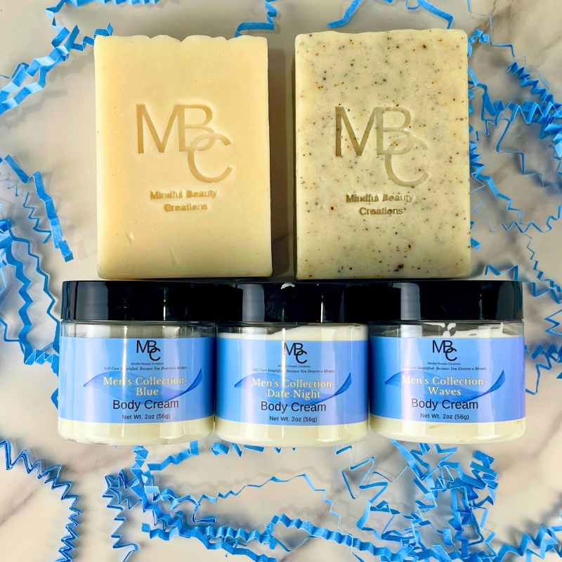 A gift set of body care products from Mindful Beauty Creations, including two bars of soap  and three jars of Men's Collection Body Cream, arranged on a marble surface with blue paper crinkle decorations.