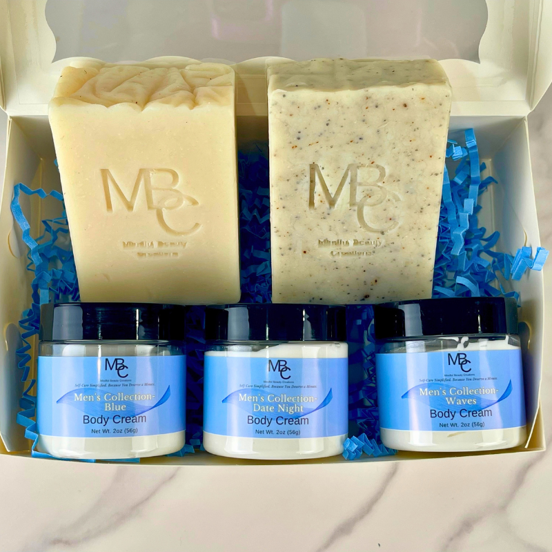 A boxed gift set of men's skincare and soap bars from Men's Collection by Mindful Beauty Creations. The set includes two handmade soap bars and three jars of body cream arranged in blue paper shred inside an open white gift box.