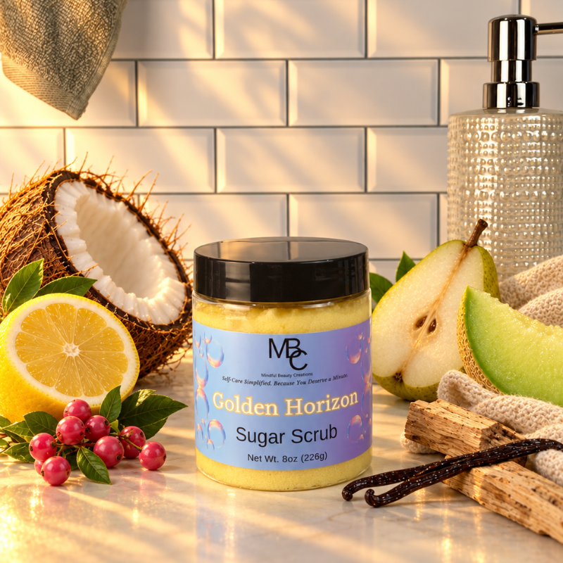 A jar of MBC 'Golden Horizon' sugar scrub sits on a marble countertop surrounded by its scent ingredients: a halved coconut, a lemon slice, green berries, a pear slice, vanilla beans, and a textured soap dispenser in the background against a white subway tile wall.