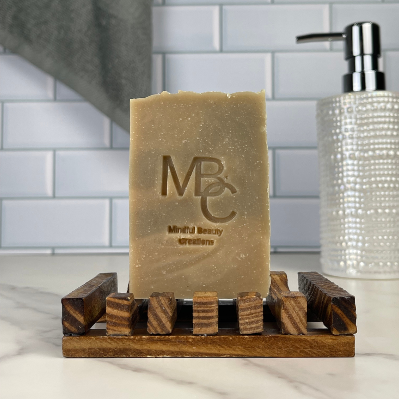 Bar of soap on a wooden soap dish with 'MBC' branding in a bathroom setting.