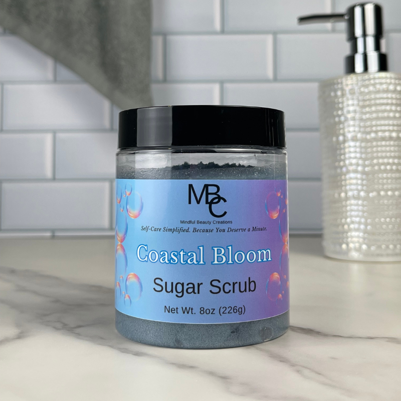 Coastal Bloom Sugar Scrub jar on a bathroom counter with a soap dispenser in the background.
