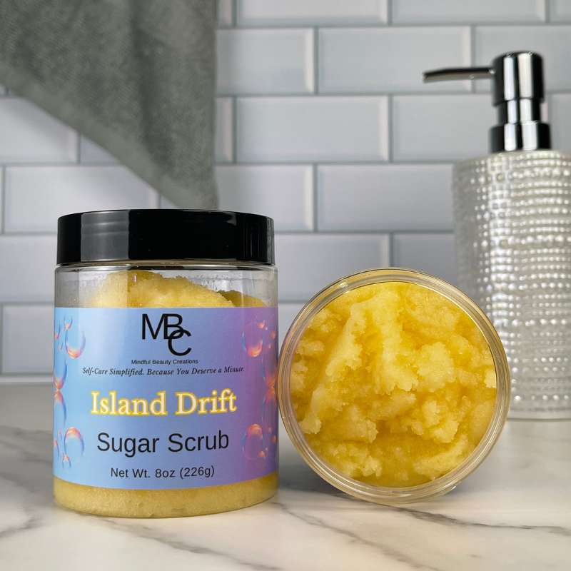 Island Drift Sugar Scrub jar with open lid on a marble surface with a tiled wall background.