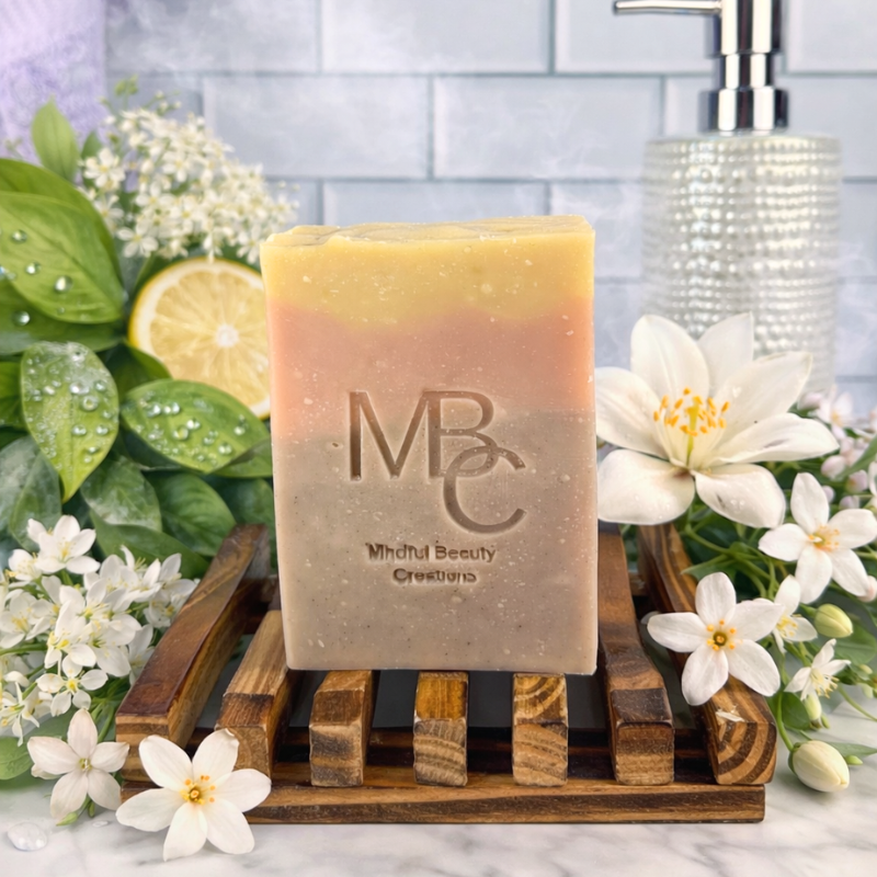Yellow, pink, and purple Bar of soap with 'MBC' branding on a wooden soap dish, surrounded by flowers and greenery.